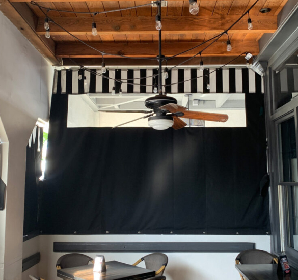 Black outdoor curtain beneath a striped awning, Orange County