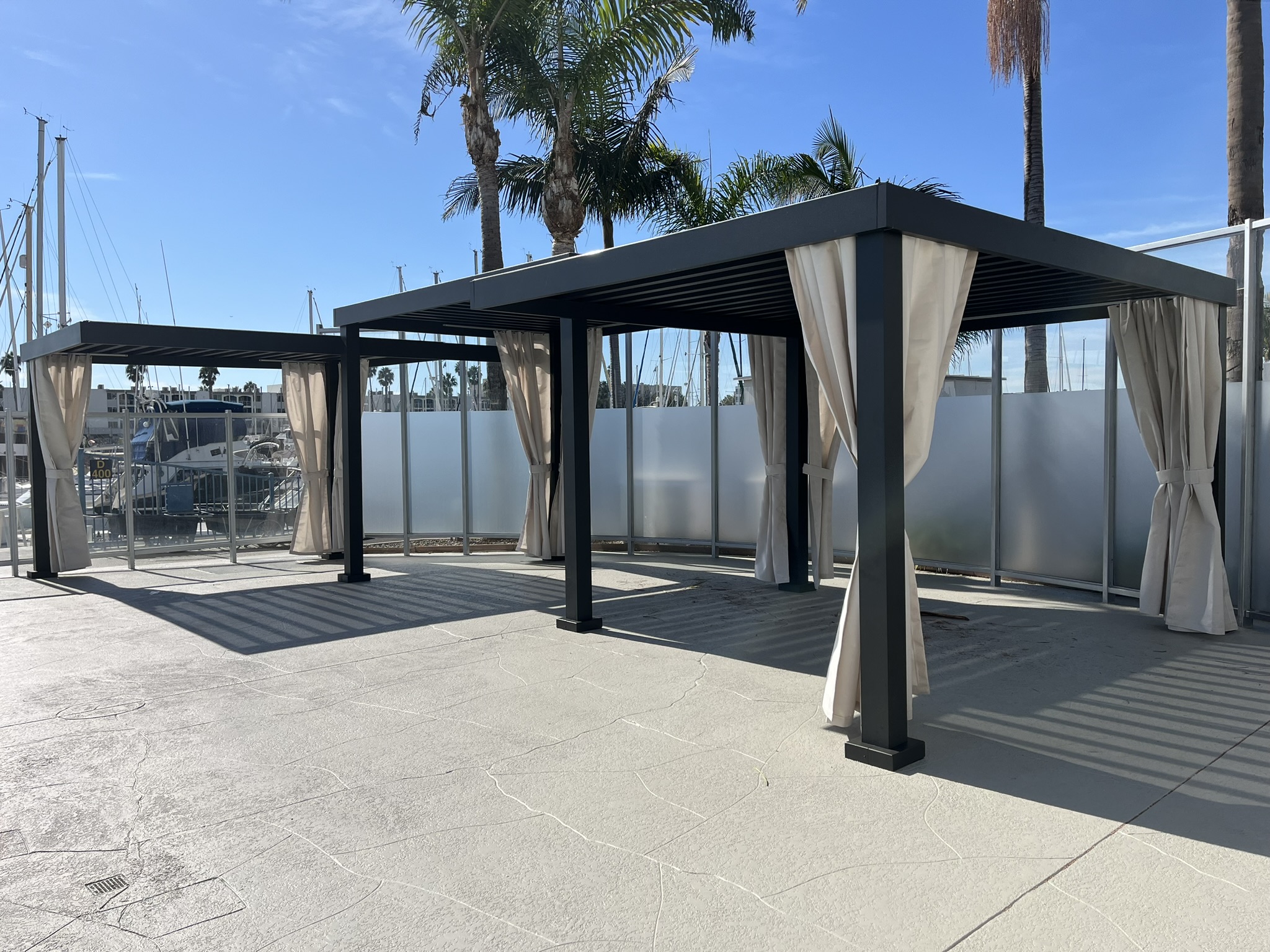Dark metal pergola with a louvered cover and curtains at Del Rey Yacht Club