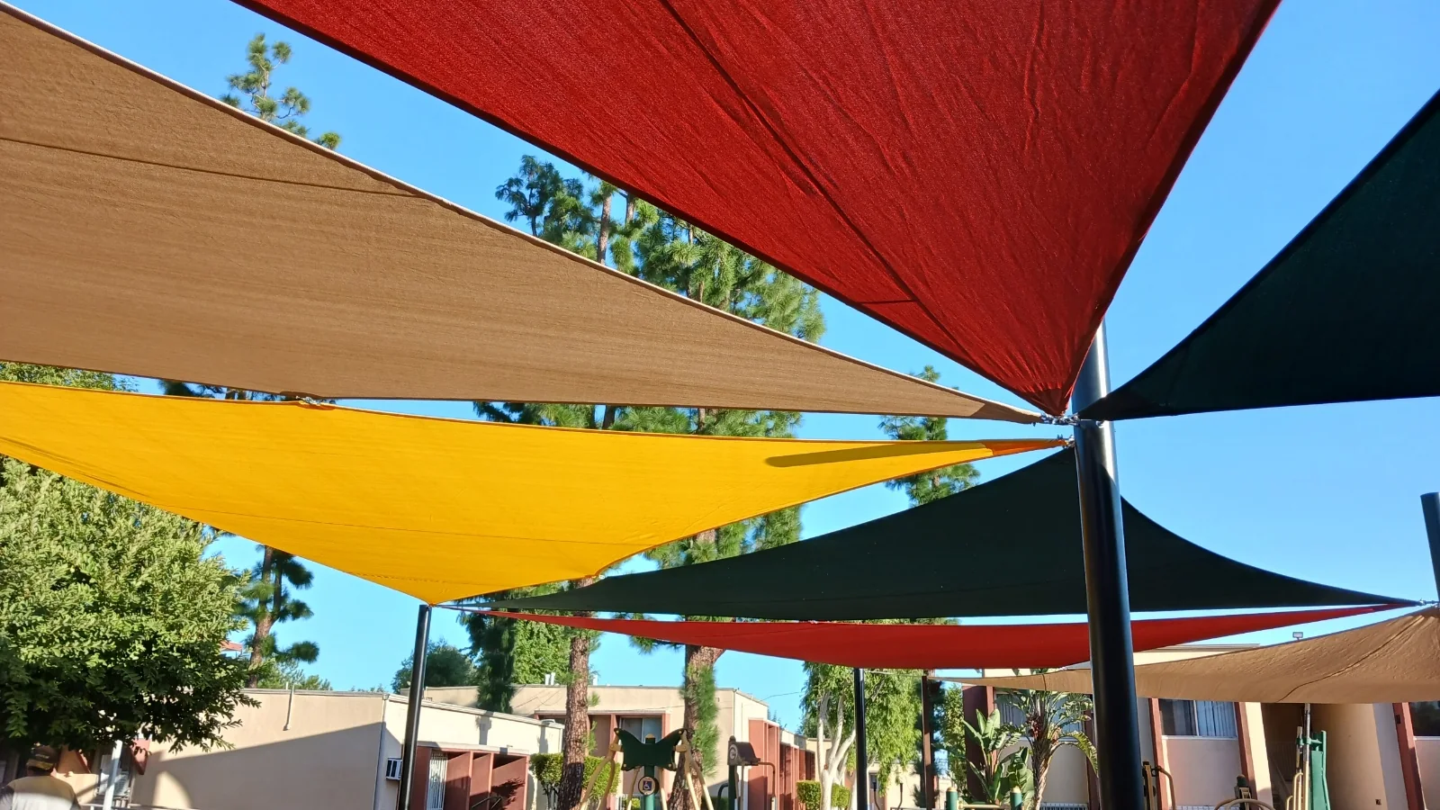 Overlapping red, yellow, tan and green shade sails installed over a public park area in Sylmar