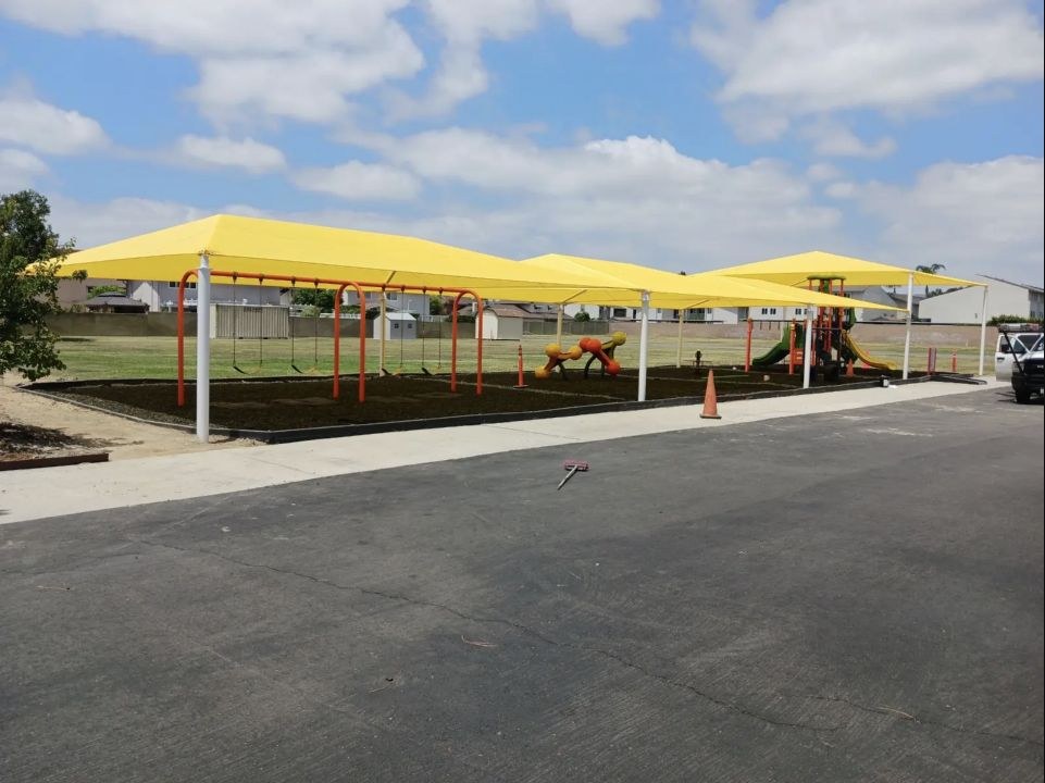 Yellow hip-roof shade canopies covering outdoor activity areas at a Cypress school