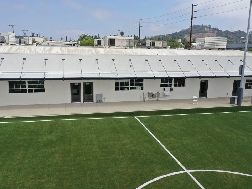 Long metal canopy with translucent polygal panels beside a school field