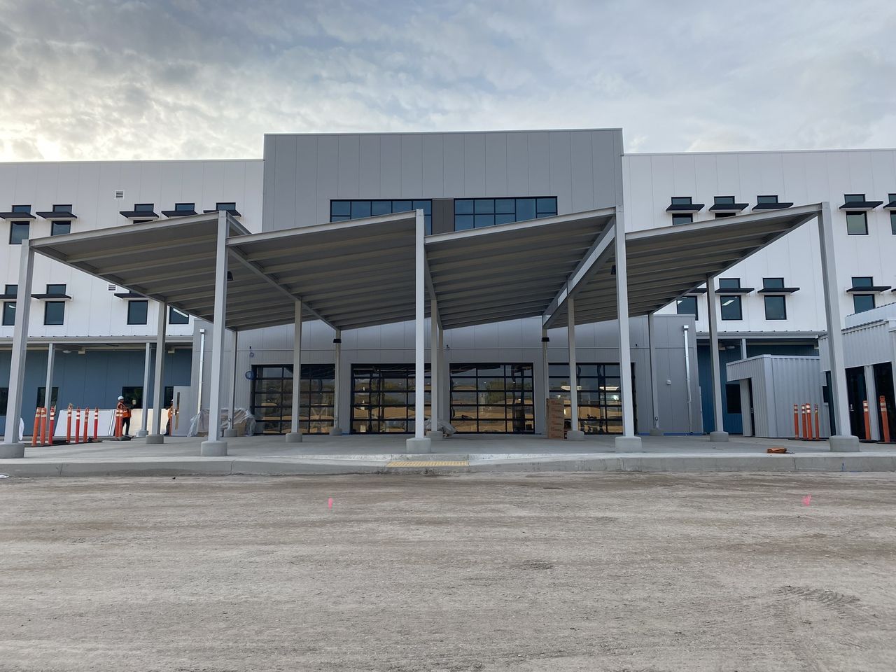 Metal canopy with four roof sections on white columns in front of glass roll-up doors at a gray and white commercial building