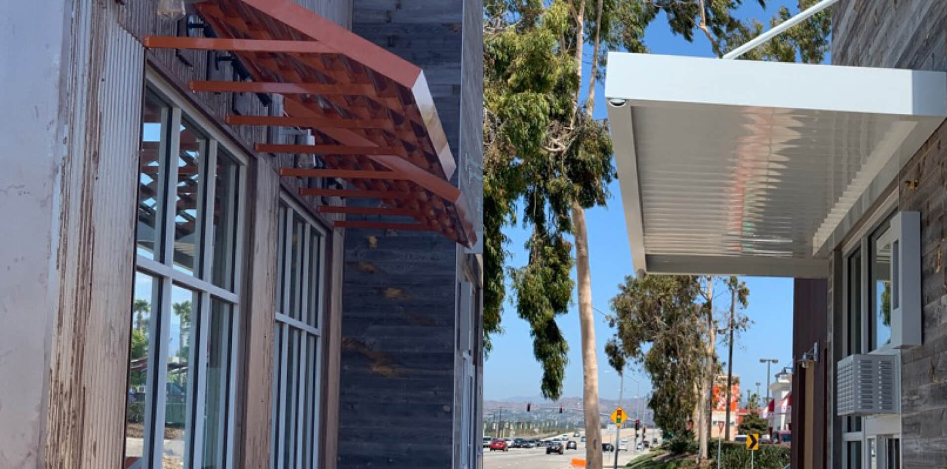 Red open metal trellis and white solid metal canopy installed on a commercial building